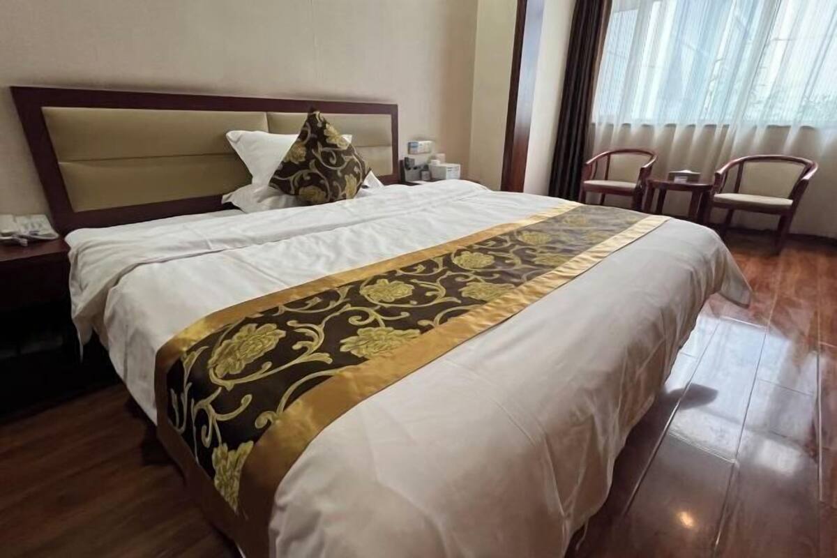 Une chambre d’hôtel avec un grand lit, une table de chevet, une chaise et une fenêtre avec des rideaux.