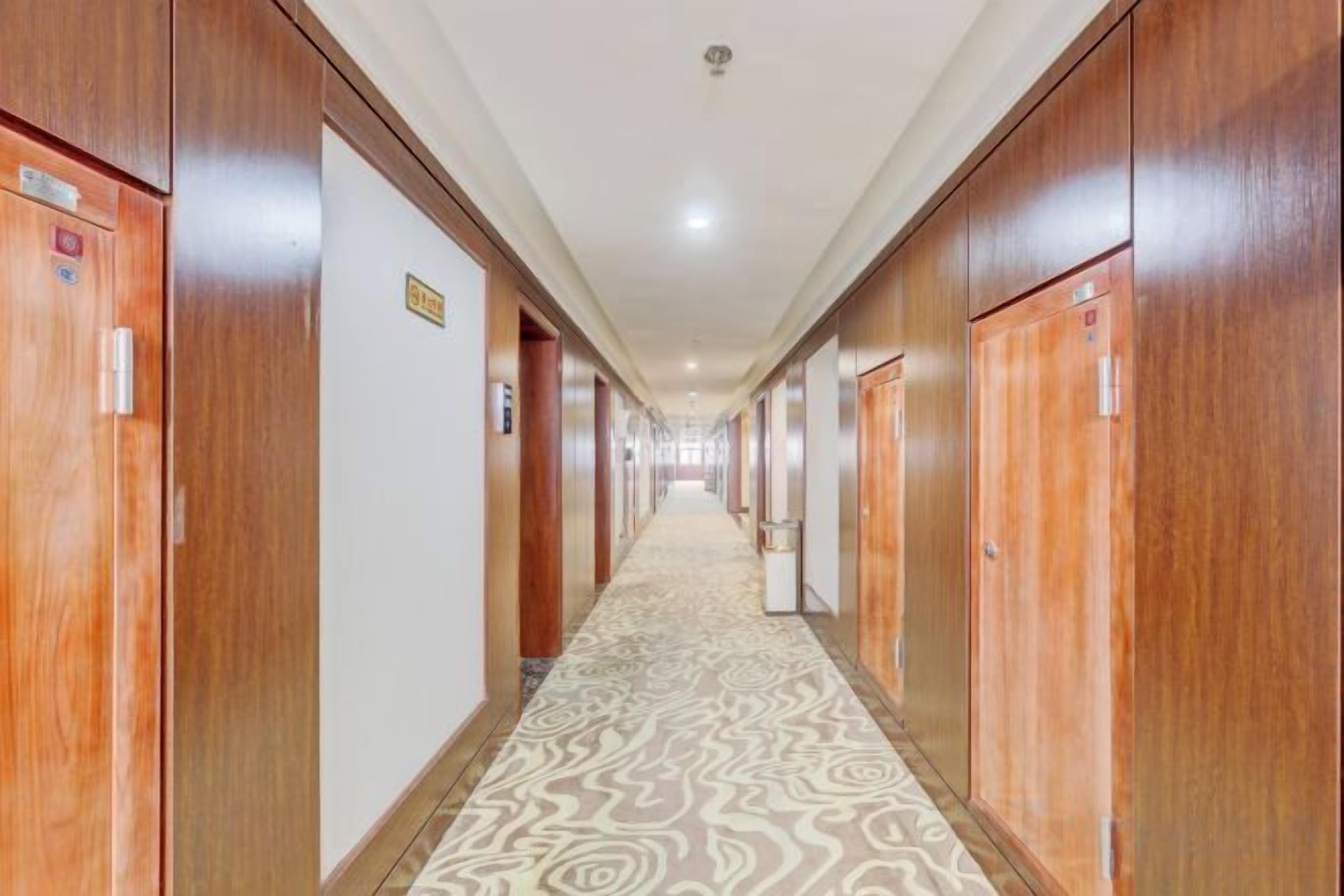 A hotel corridor with wooden doors, a patterned carpet, and a sign indicating a room number.