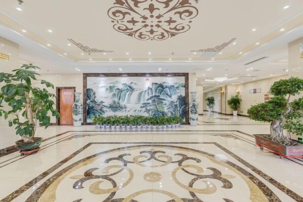 A spacious lobby with a large mural, potted plants, and a marble floor.