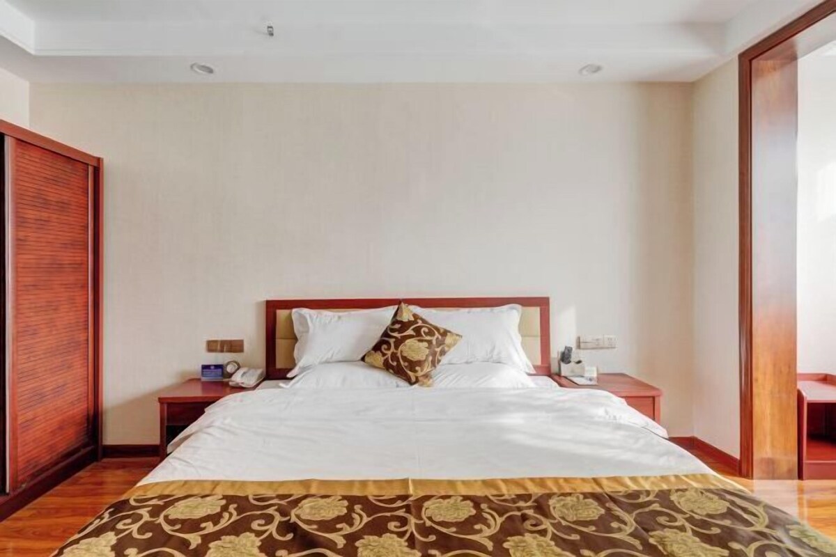 Une chambre d’hôtel avec un grand lit, une tête de lit en bois, deux tables de chevet et une armoire.
