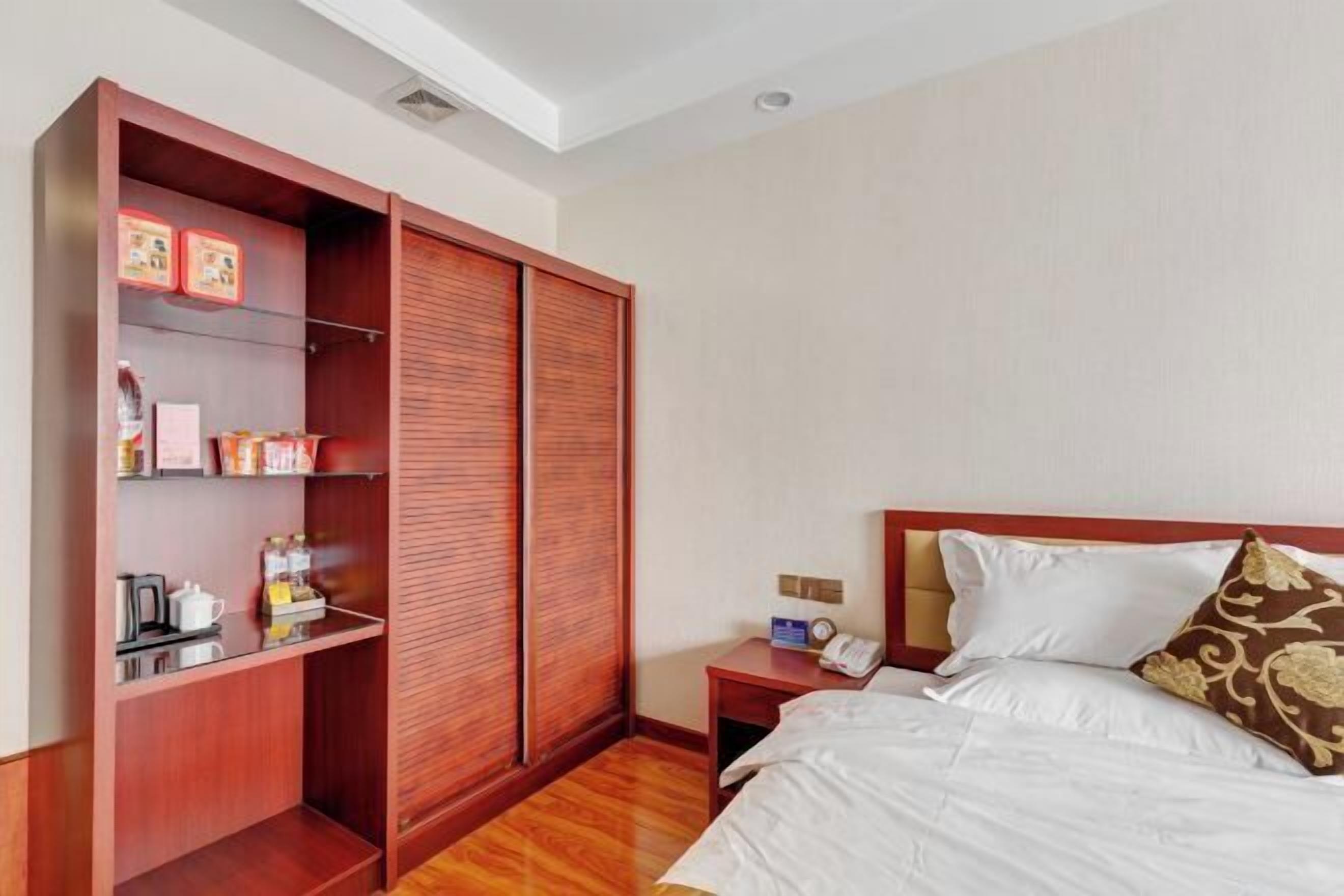 Habitación de hotel con armario de madera, cama con ropa de cama blanca, mesita de noche con teléfono y estante con artículos de aseo.