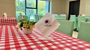 A dining area with red and white checkered tables, green chairs, and a flower vase on one table. - Gaoqing Shuangchuangyuan Hotel (Gaoqing)
