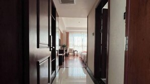 A hotel corridor with a polished floor, wooden doors, and a bed with a white headboard in the background. - Gaoqing Shuangchuangyuan Hotel (Gaoqing)
