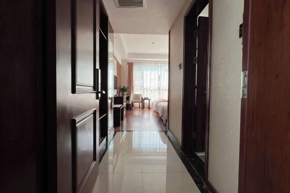 A hotel corridor with a polished floor, wooden doors, and a bed with a white headboard in the background. - Gaoqing Shuangchuangyuan Hotel (Gaoqing)