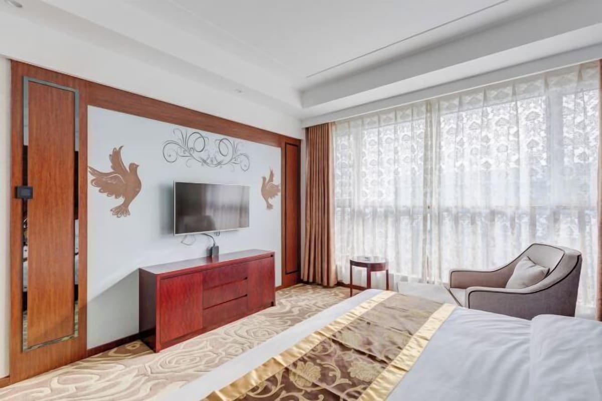 Une chambre d’hôtel avec un lit, un téléviseur posé sur une commode en bois, une petite table et une chaise.