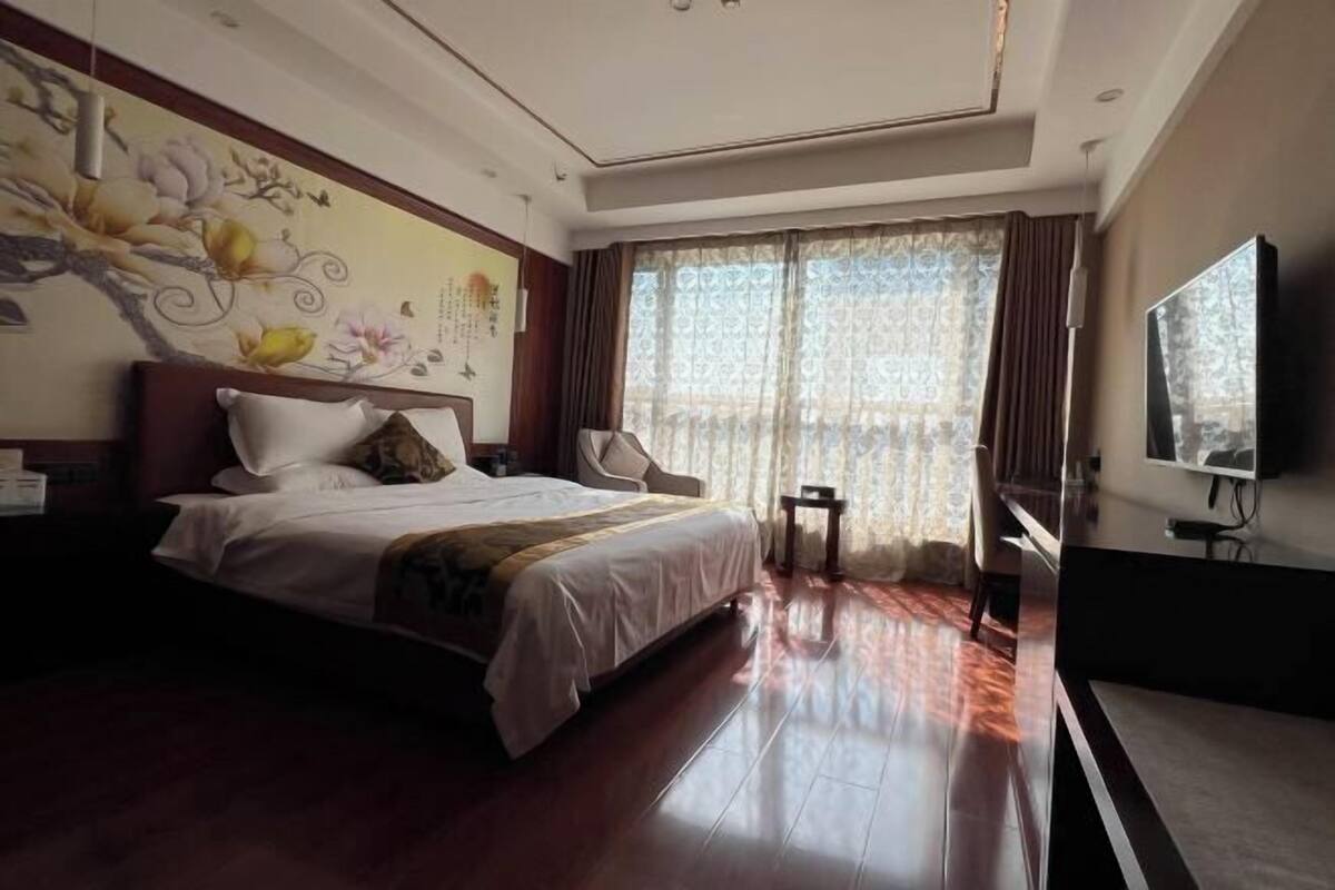 Une chambre d’hôtel avec un grand lit, une télévision, un bureau et une fenêtre avec des rideaux.