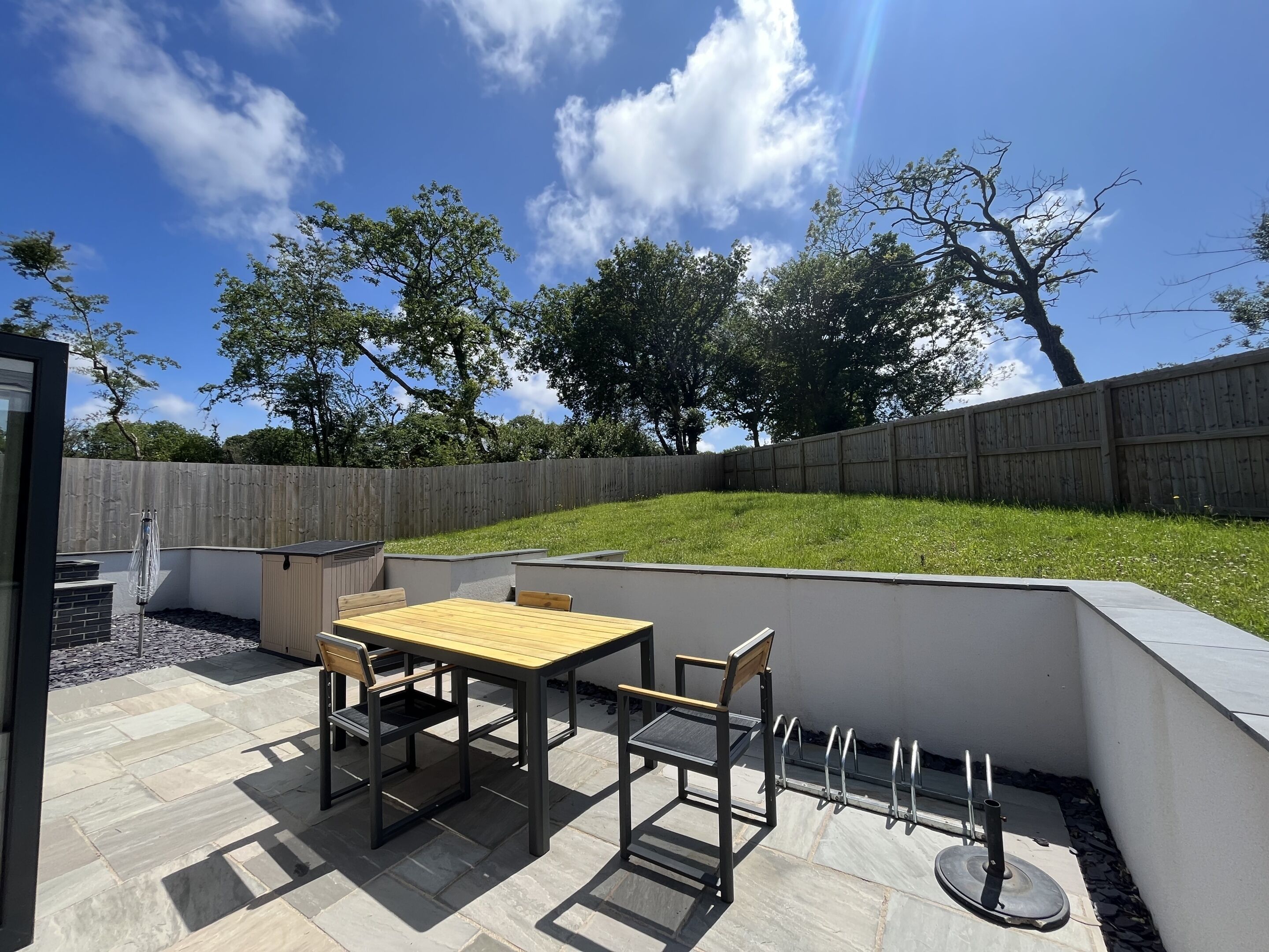 An outdoor patio with a table and chairs, a barbecue grill, and a stone-tiled floor.