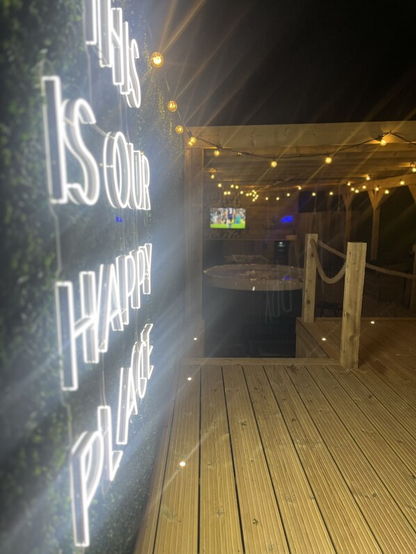 An outdoor wooden deck with a neon sign reading "THIS IS OUR HAPPY PLACE."
