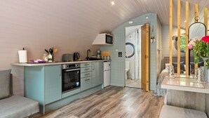 Cocina compacta con microondas, horno y lavabo, sofá gris y techo de madera.