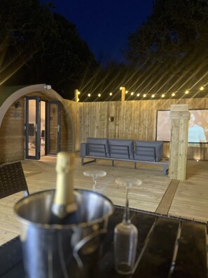 An outdoor seating area with a wooden deck, a bench, and a table with a bottle and glasses.
