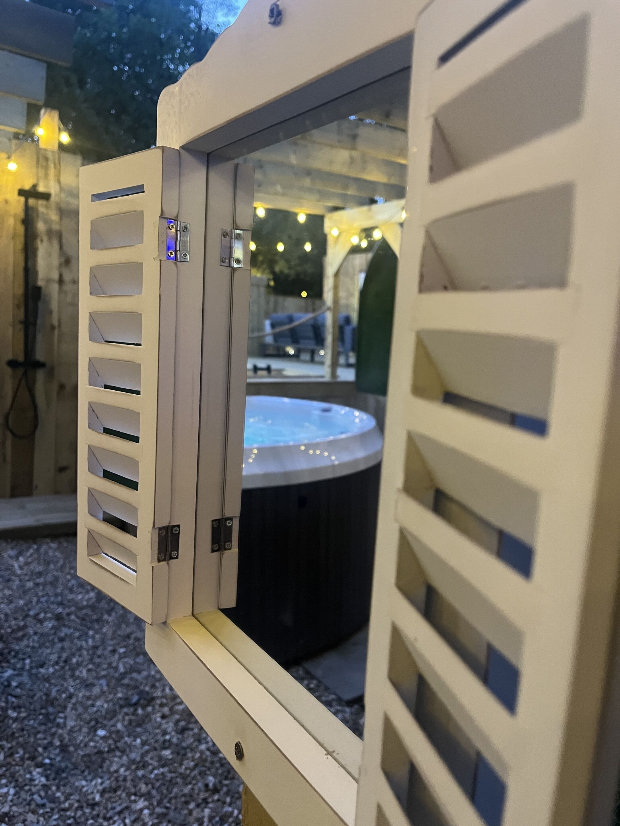 Un bain à remous doté d’une fenêtre, entouré de lumières extérieures et bordé d’une zone recouverte de gravier.