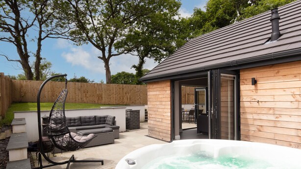 A hot tub in a backyard with a wooden deck, a swing chair, and a patio area.