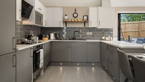 A modern kitchen with grey cabinets, a built-in oven, microwave, and sink. There is a wooden shelf above the sink with decorative items.