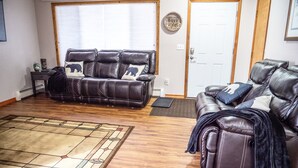 A living room with a brown leather sofa, a matching ottoman, and a patterned rug. - Central Home: Yard with Mountain Views, 3bdrm (Anchorage)