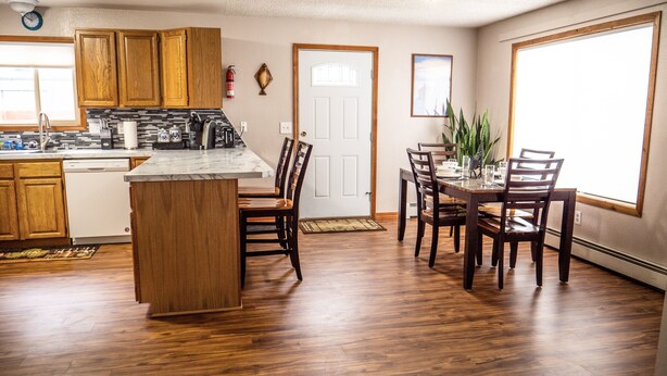 A kitchen with wooden cabinets, a marble countertop, and a dining area with wooden chairs and a table. - Central Home: Yard with Mountain Views, 3bdrm (Anchorage)
