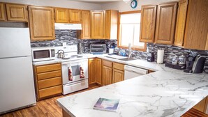A kitchen with wooden cabinets, a white refrigerator, a microwave, a toaster, and a marble countertop. - Central Home: Yard with Mountain Views, 3bdrm (Anchorage)