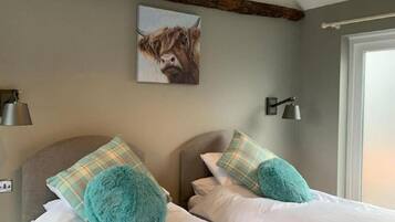 Une chambre à coucher avec un lit, deux oreillers, une couverture, un tableau représentant une vache et une fenêtre.