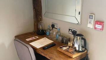 A small, neatly organized workspace with a wooden desk, a chair, a kettle, a coffee maker, and a mirror on the wall.