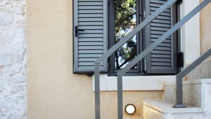 Een trap met stenen treden en metalen leuningen, leidend naar een raam met luiken.