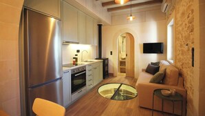 Een compacte keuken met moderne apparaten, een eetgedeelte met een glazen tafel en een gezellige zithoek met een bank en een klein bijzettafeltje.