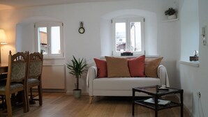 A living room with a white sofa, wooden chairs, a coffee table, and a potted plant. - The Jura House 1540 - a vacation in a monument on the Danube Cycle Path (Pförring)