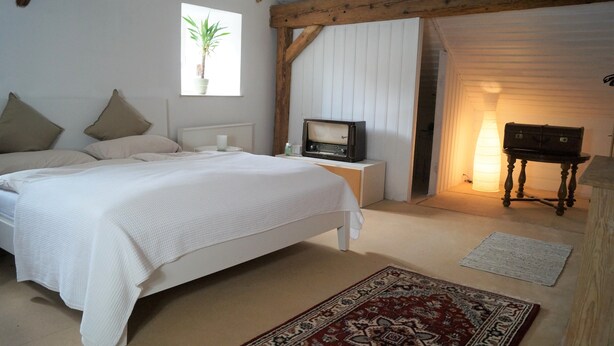A bedroom with a large bed, a small table with a radio, a lamp, and a wooden cabinet. - The Jura House 1540 - a vacation in a monument on the Danube Cycle Path (Pförring)