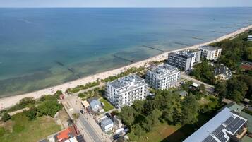 Une vue aérienne d’une zone côtière, avec une plage, plusieurs immeubles à étages et une vue dégagée sur la mer.