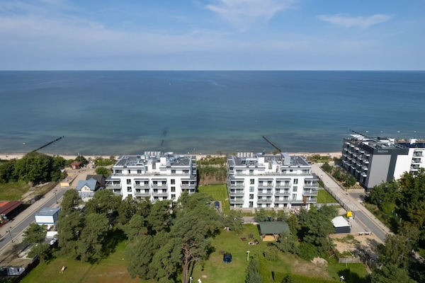 An aerial view of a seaside neighborhood, highlighting modern architecture and lush greenery.