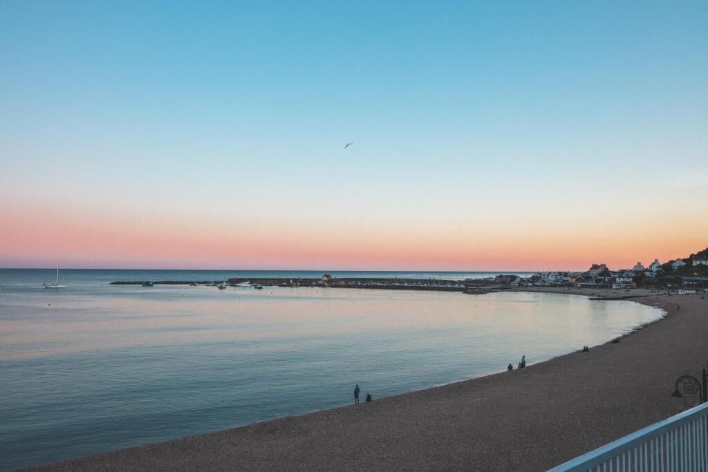 Una playa con aguas tranquilas, cielo despejado y una línea de costa distante con edificios.