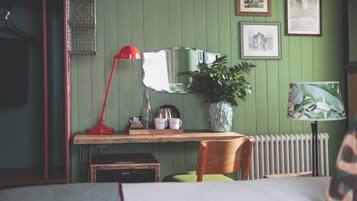 A room with a wooden desk, a red lamp, a mirror, a radiator, and framed pictures on the wall.
