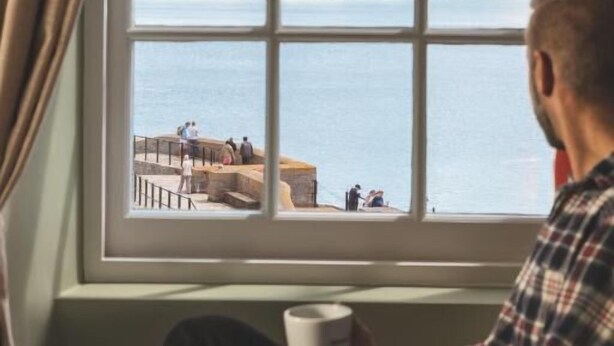 A person sitting by a window with a view of a coastal area. - Rock Point Inn (Lyme Regis)