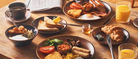 A breakfast table with various dishes, a newspaper, and a glass of orange juice.