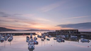 A marina with boats docked, a building with a flat roof, and a calm water body reflecting the sky. - Rock Point Inn (Lyme Regis)