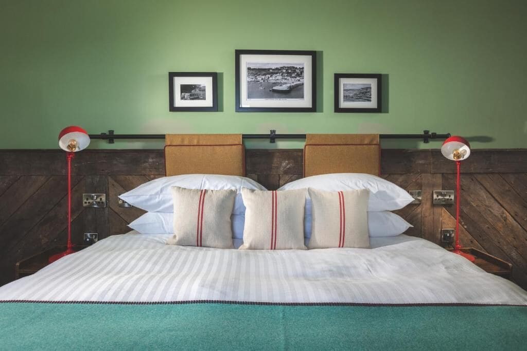 Una cama con colcha a rayas, dos almohadas y un cabecero de madera. Encima de la cama, hay tres cuadros enmarcados en la pared.