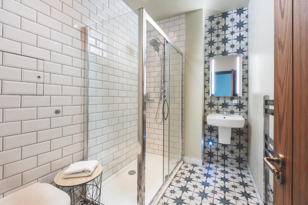 Un bagno con piastrelle bianche a metro, una doccia con porta in vetro, un lavabo con specchio e un pavimento a motivi stellari.