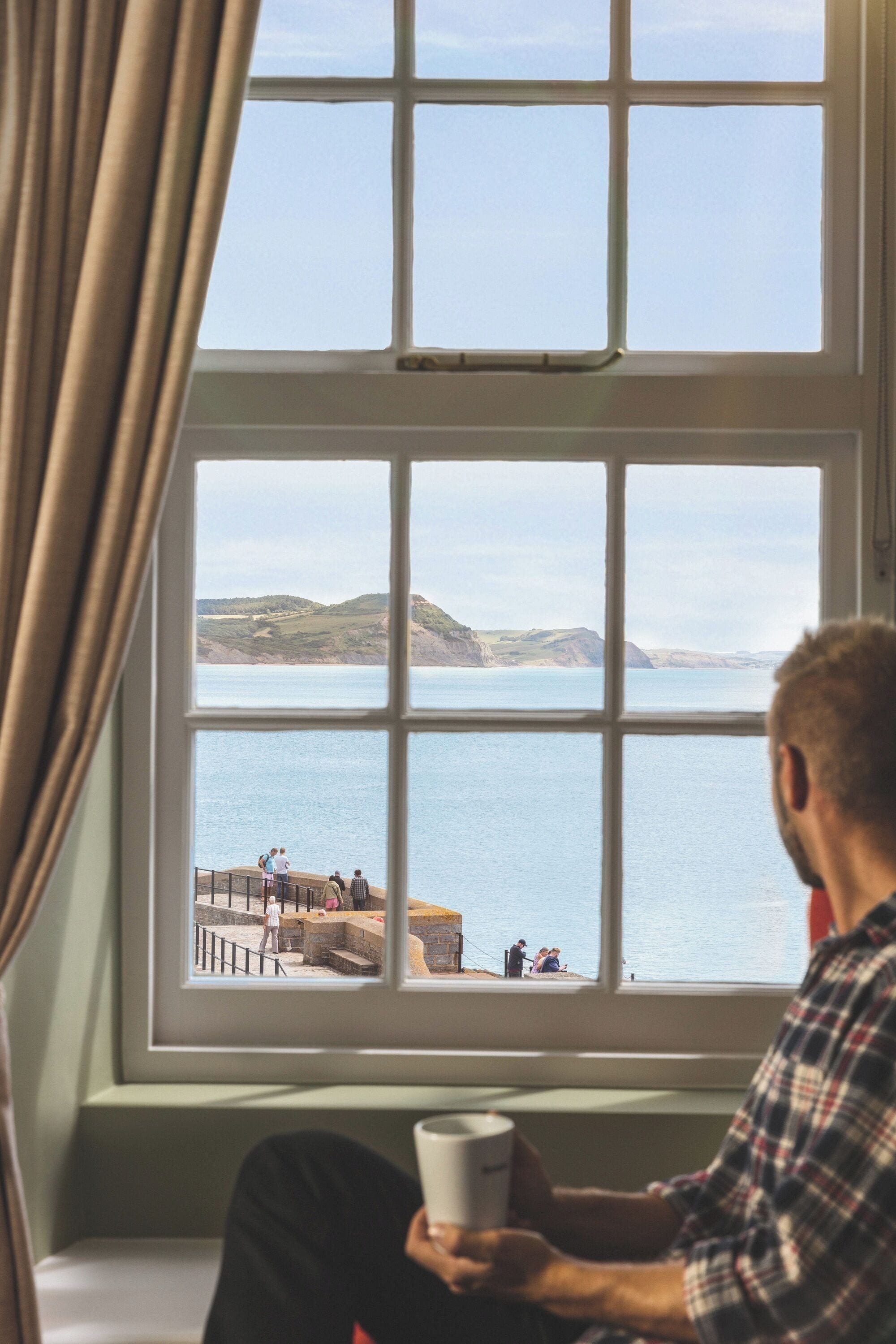 A person sitting by a window with a view of a coastal landscape.
