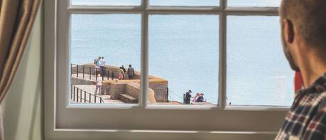 A person sitting by a window with a view of a coastal landscape.