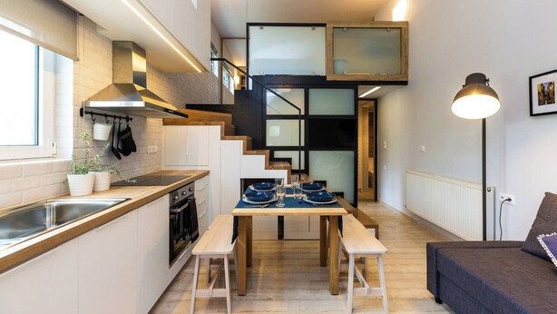 A compact kitchen with a dining area, a staircase, and a sofa.