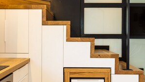 A modern kitchen with white cabinetry, wooden accents, and a black staircase.