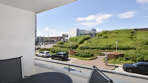 Vista dalla finestra su una strada con auto parcheggiate lungo il lato, un edificio dal design moderno e una collina verde sullo sfondo.