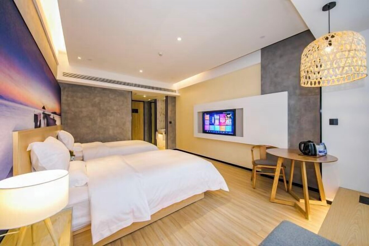 A modern hotel room with a large bed, a TV mounted on the wall, a wooden table, and a unique hanging light fixture.