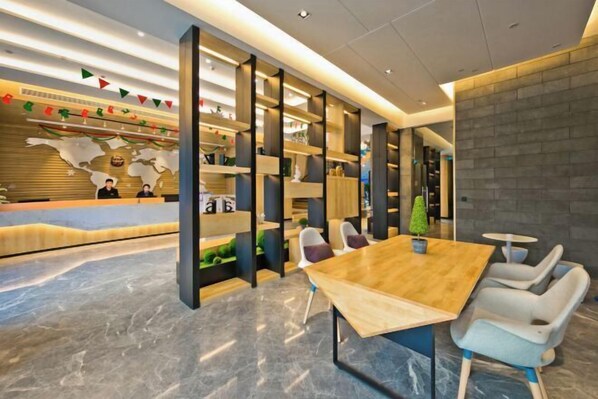 A modern reception area with a wooden reception desk, a large wooden table, and white chairs. There are shelves with decorative items and a small potted plant.