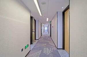 Un pasillo de hotel con piso alfombrado, puertas a ambos lados y una lámpara en el techo.