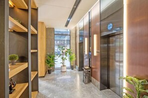 A modern hotel lobby with a marble floor, wooden shelving, potted plants, and an elevator. - Tuke China Hotel (Fuding Central Plaza) (Fuding)
