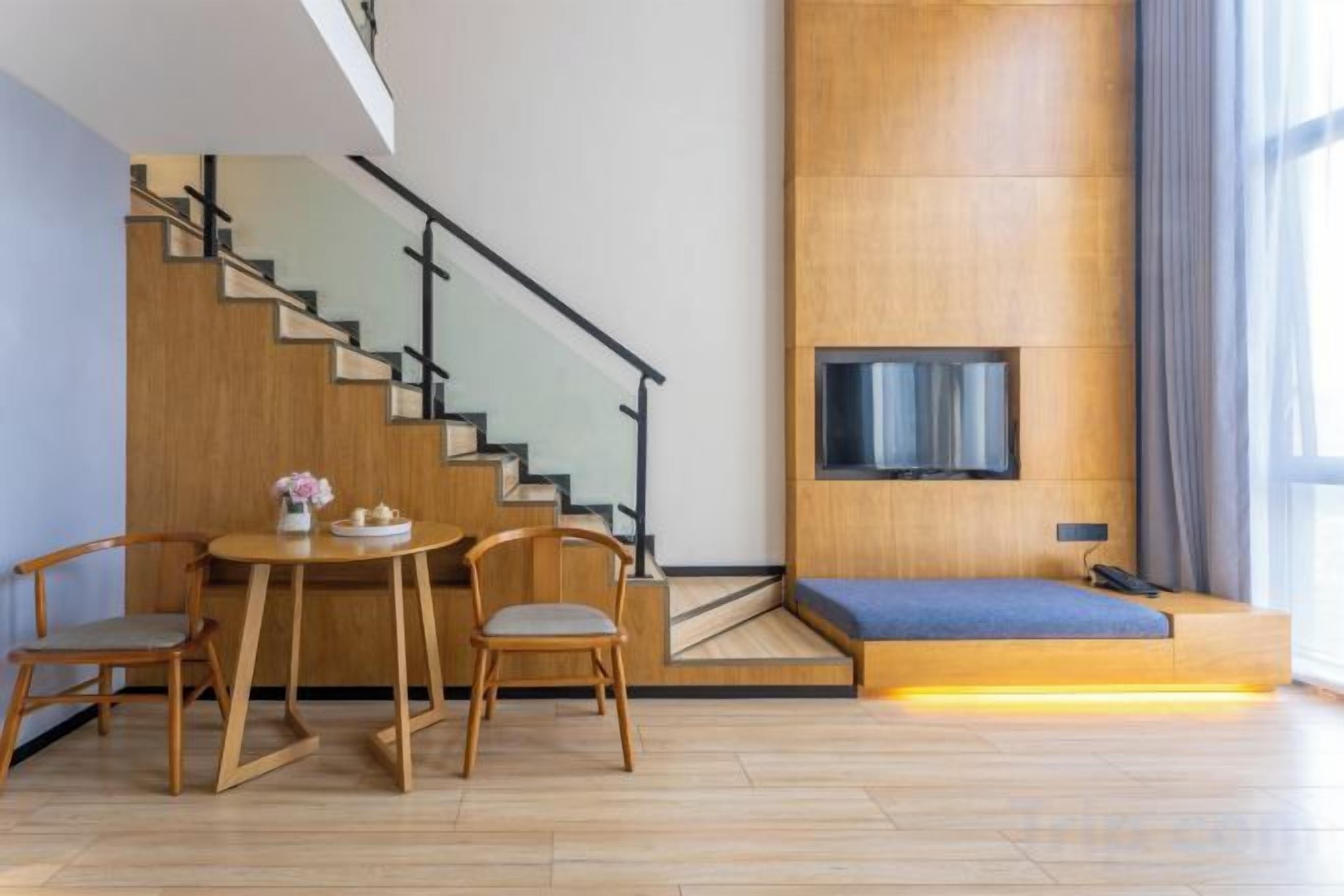 A modern living space with a staircase, a dining area with a table and chairs, a sofa, and a flat-screen TV mounted on the wall.