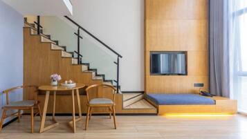 A modern living space with a staircase, a dining area with a table and chairs, a sofa, and a flat-screen TV mounted on the wall.