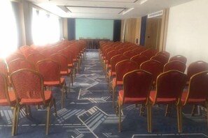 Sala de conferências com fileiras de cadeiras e um palco na frente.