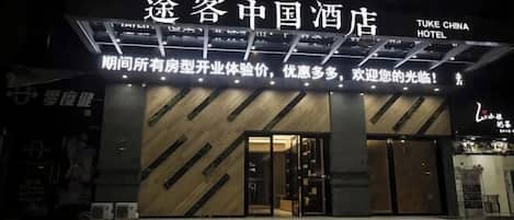 A hotel entrance with a modern design, featuring a prominent sign with Chinese characters and English text.