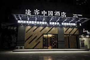 Entrada de hotel com design moderno, destacando uma placa com caracteres chineses e texto em inglês.