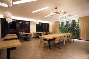Un comedor moderno con mesas y sillas de madera, ventanas amplias y una pared verde.